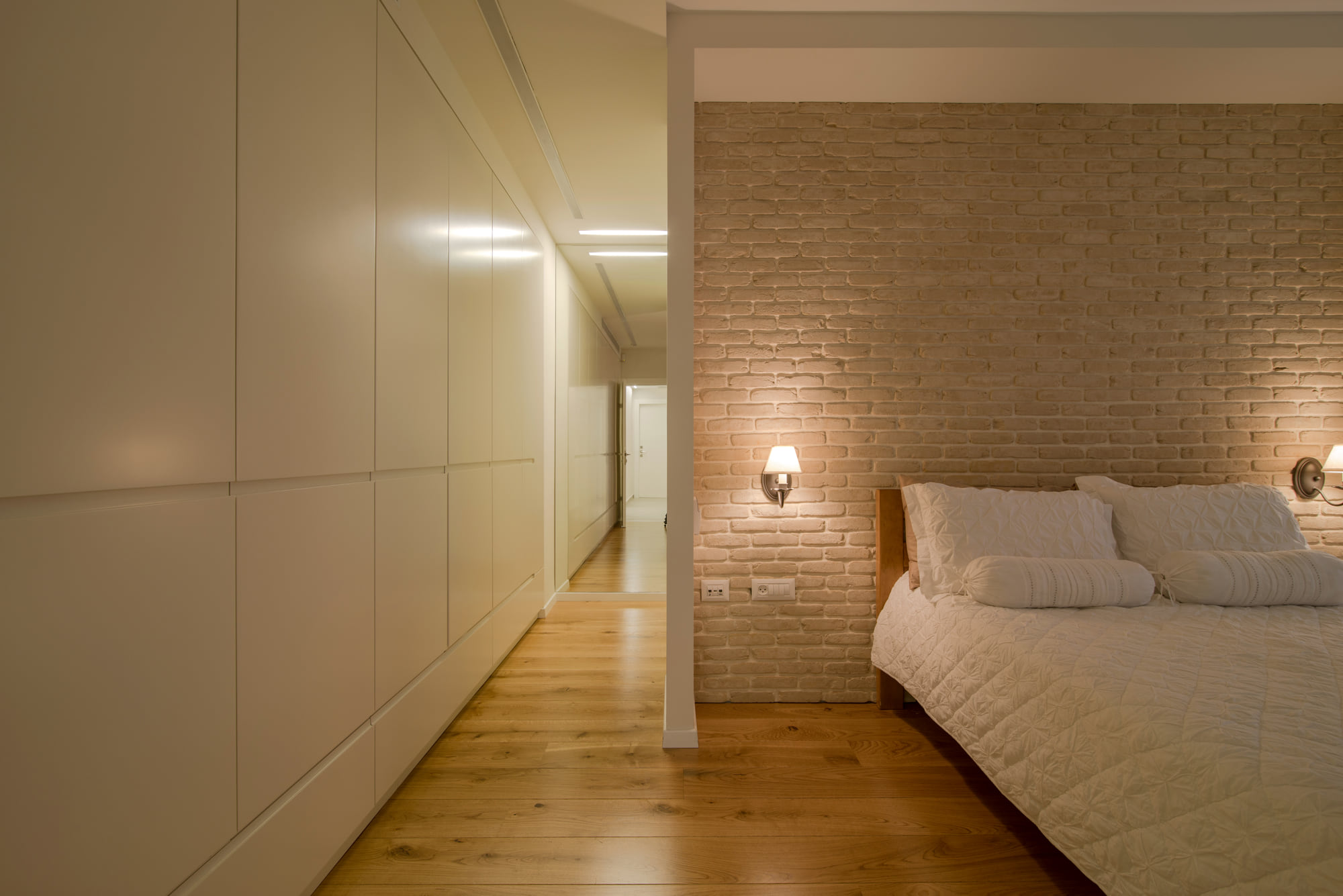 A smooth run of wardrobes the whole length of the corridor, and opposite it the bedroom with its reclaimed brick wall