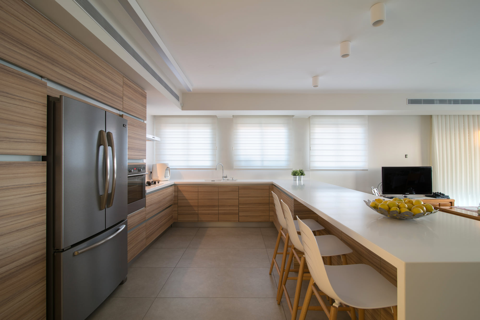 The kitchen — pale timber joinery along the wall, and facing it a long white worktop that doubles as a bar