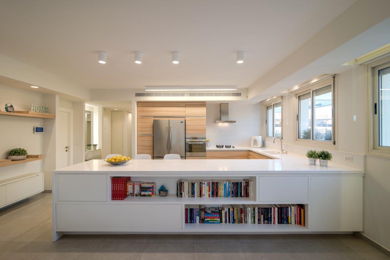The open plan — the white island with a bookcase recessed into its face, and the timber kitchen behind it