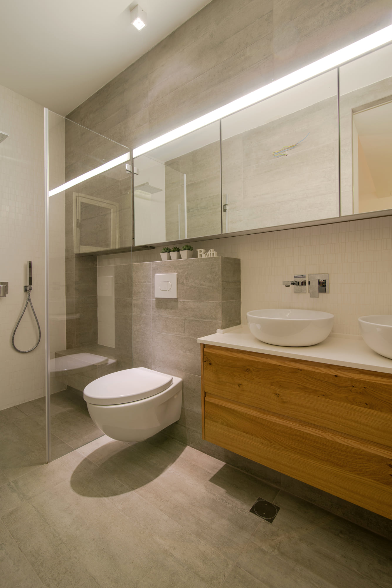 The bathroom off the master bedroom — a wall-hung oak unit with two countertop basins, and an open shower beside it