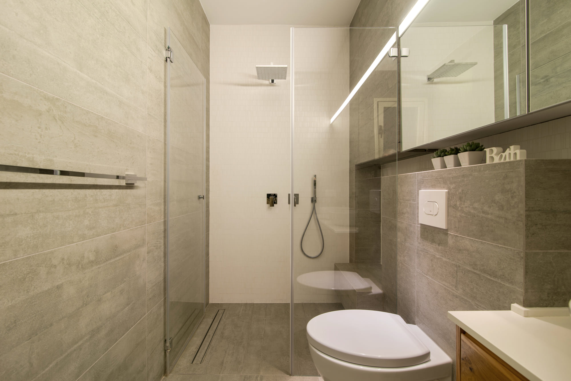 The bathroom off the master bedroom — a frameless glass shower, grey stone cladding and a light slot running the length of the mirror
