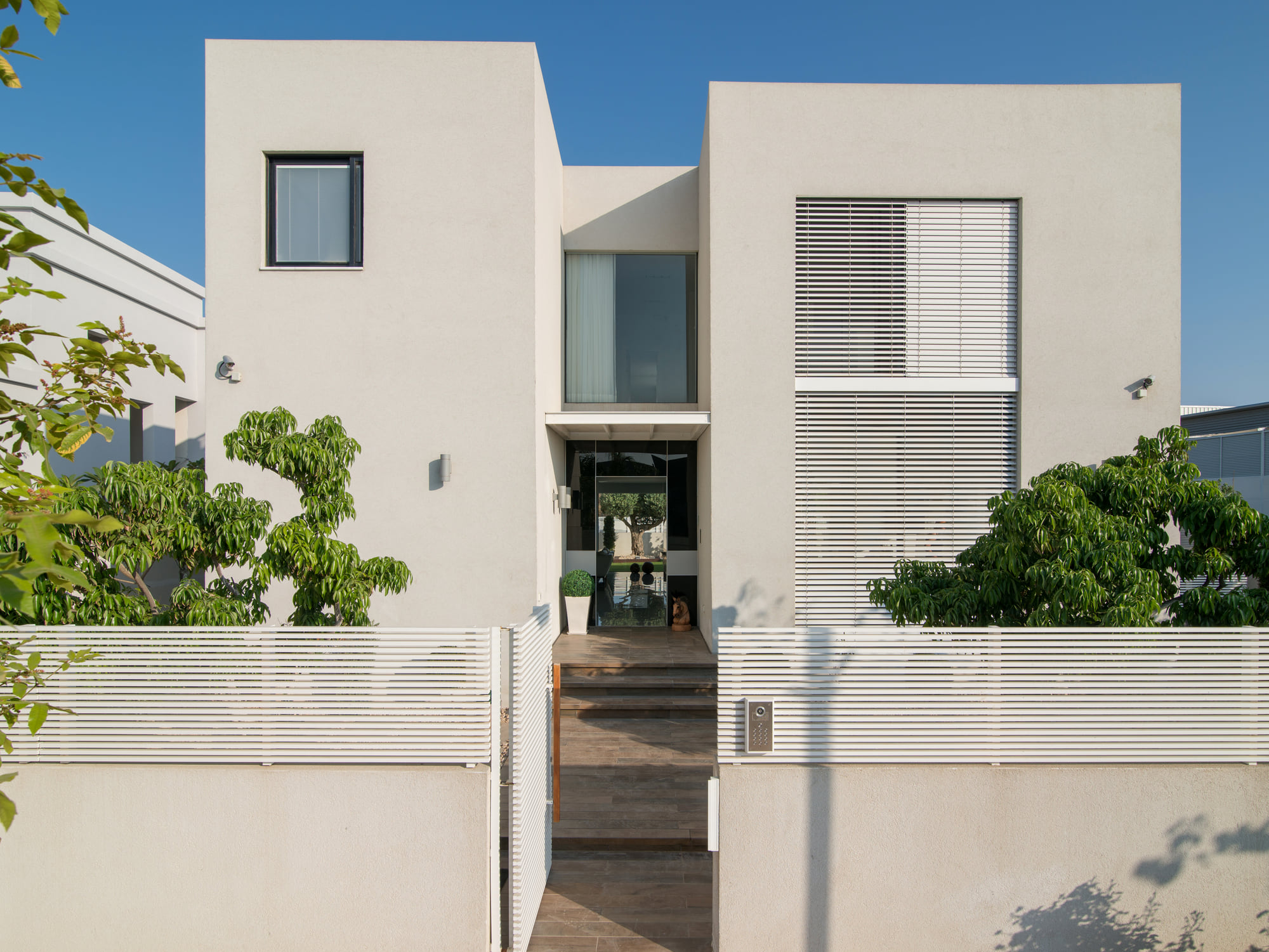 The front of the house — white volumes, louvred shutters and a shaded entrance