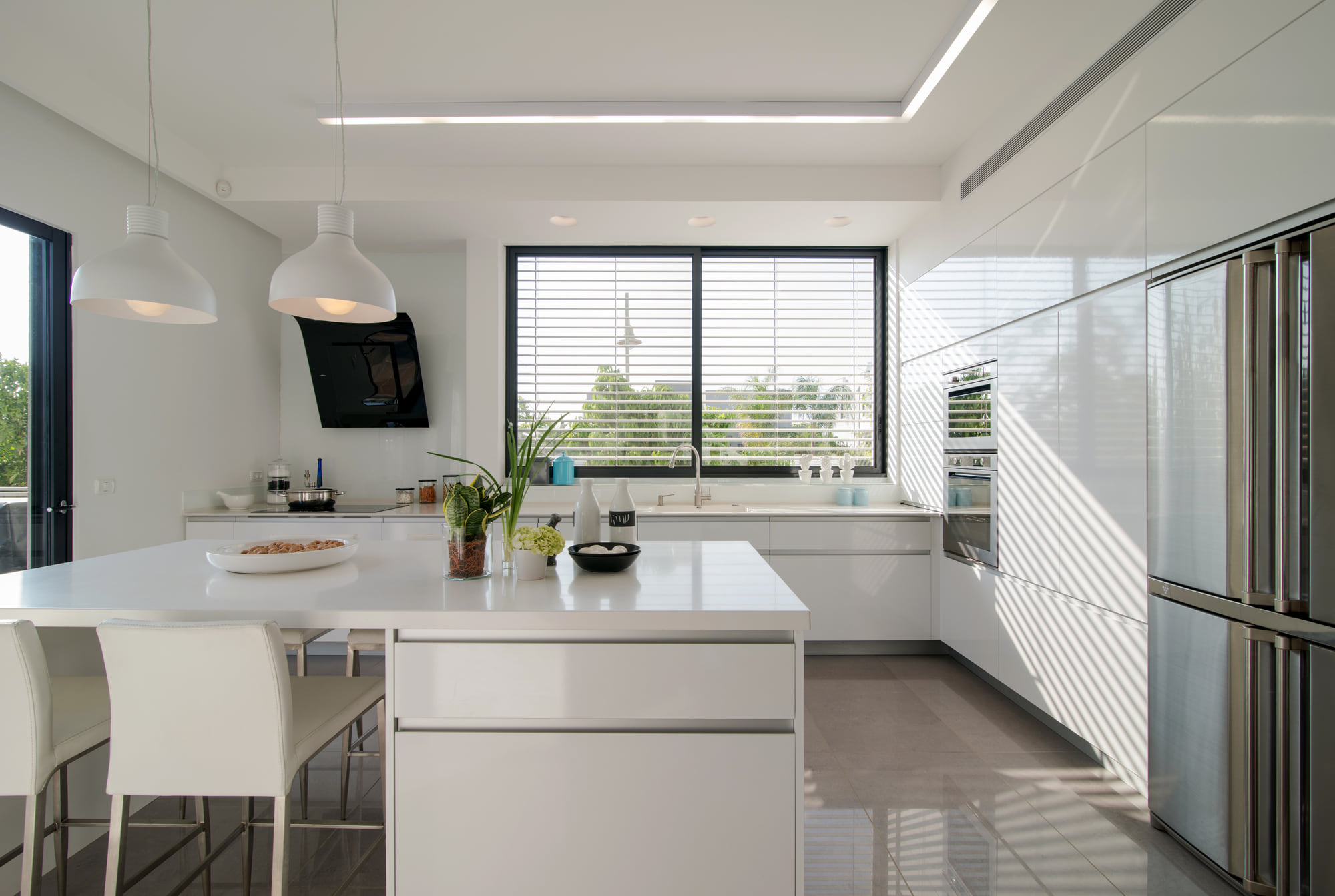 The kitchen — a white island with stools and pendant lamps, against a louvred window