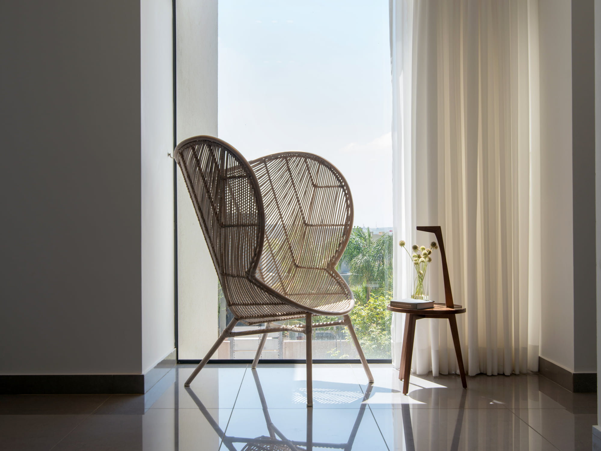 A rattan armchair facing a floor-to-ceiling window with a sheer curtain
