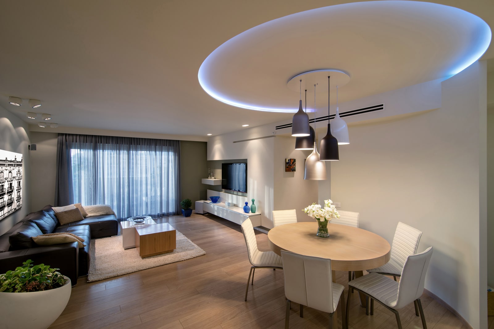 The living room and dining area in one space — a round ceiling volume with concealed lighting defines the dining area, with a cluster of pendants beneath it